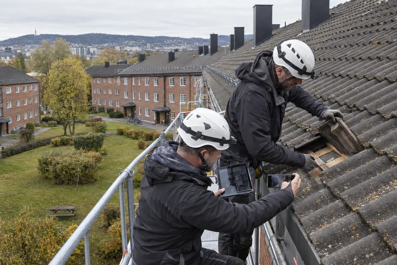 To taktekkere dokumenterer tilstanden under takstein på en boligblokk i Oslo fra et sikret stillas