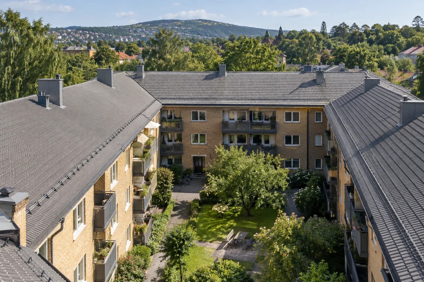 Illustrasjon: Sammenhengende boligblokker med grå tak rundt et grønt gårdsrom