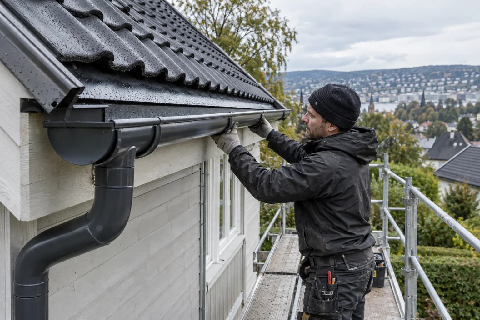Taktekker monterer en ny mørk stålrenne fra sikret stillas på en bolig i Oslo